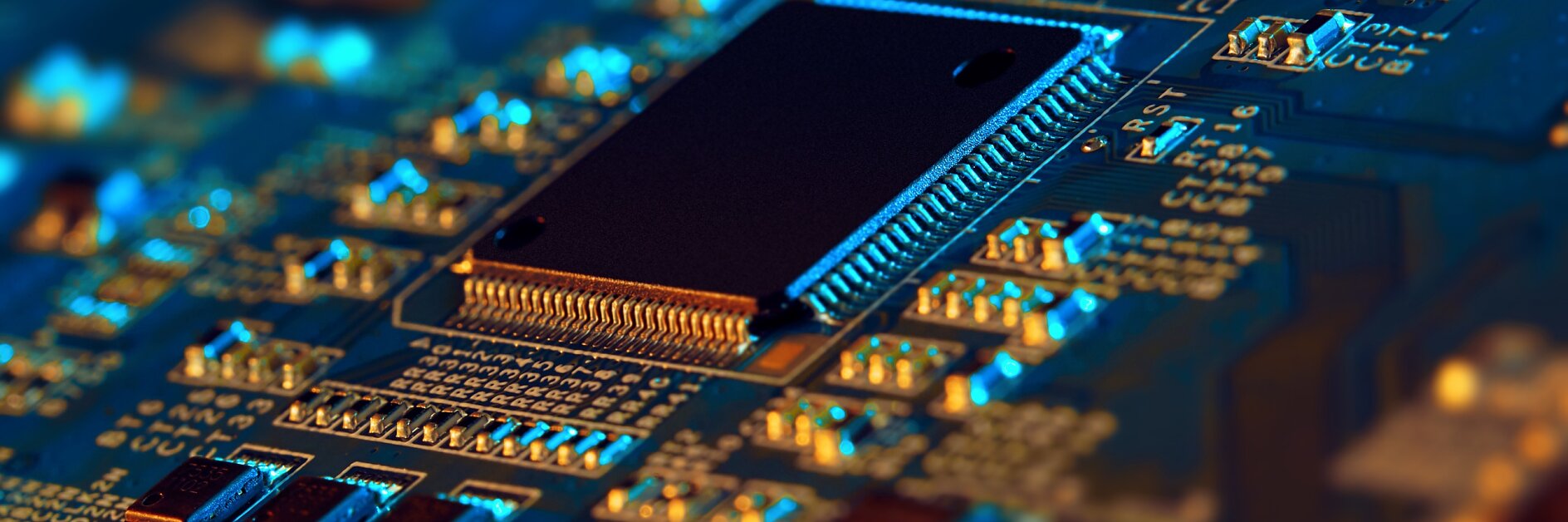 Close-up of an electronic circuit board featuring a central black microchip surrounded by various small components like resistors and capacitors. The board is illuminated with blue and orange lighting, highlighting its details.